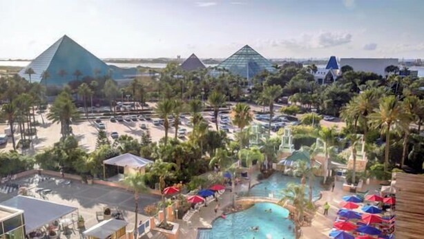 Un resort con varias construcciones en forma de pirámide, una piscina central y palmeras circundantes.