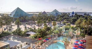 Un resort con varias construcciones en forma de pirámide, una piscina central y palmeras circundantes.