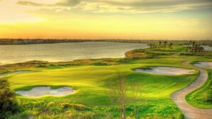 Campo de golf con búnkeres de arena, una masa de agua y un puente al fondo.