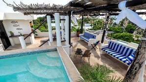 A rooftop pool area with a pool, lounge chairs, and a pergola.