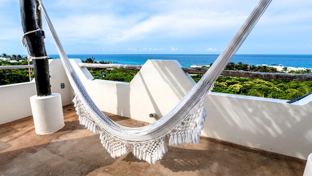 A hammock on a balcony with a view of the ocean.
