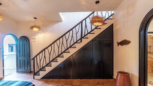 Una escalera con barandillas negras, puertas, un jarrón grande y un tapiz estampado.