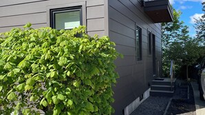 Moderni, kaksikerroksinen rakennus, jonka ulkoseinät ovat harmaat, edessä on pieni puutarha ja taivaalla on kirkas, sininen taivas.