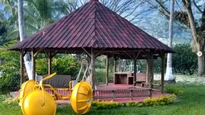 A gazebo with a metal roof and a platform, surrounded by grass and trees.