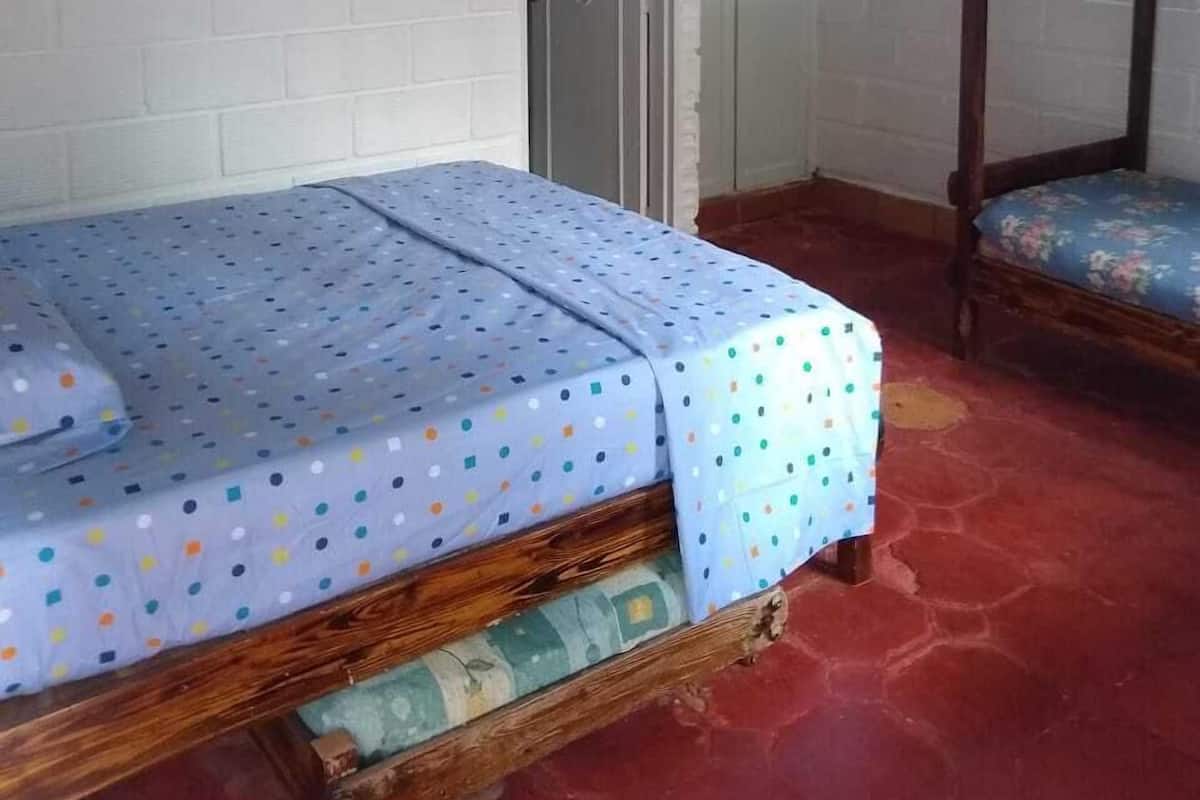A room with a wooden bunk bed, a single bed with a polka dot bedspread, a white brick wall, a door, and a framed picture on the wall.