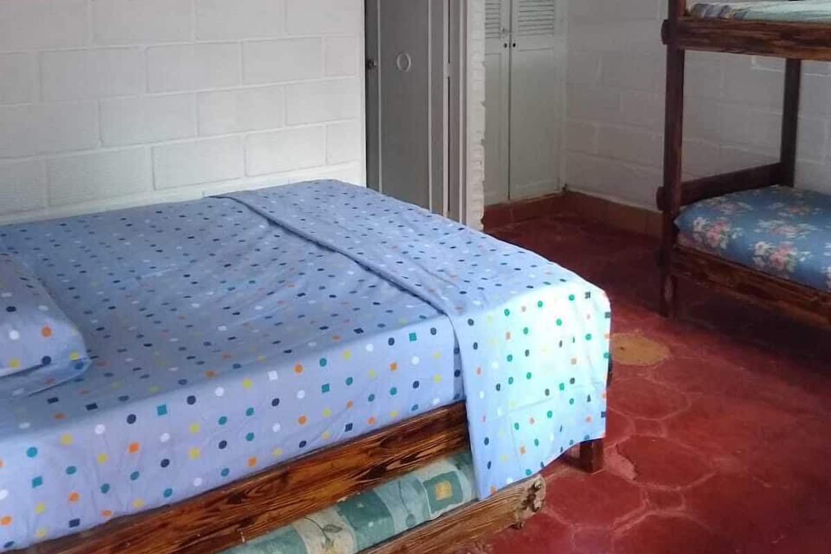A small, cozy room with a single bed, a wooden bunk bed, a white brick wall, and a door.