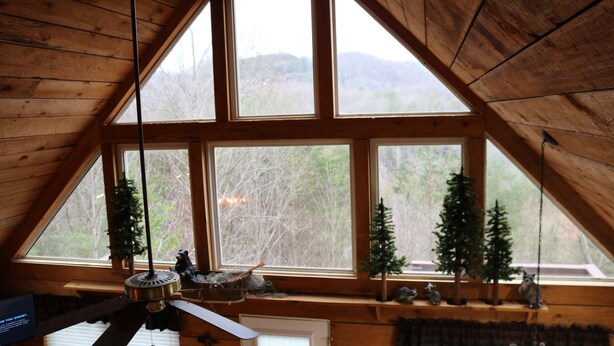 Una stanza con un soffitto in legno a falde, ampie finestre, una ventola a soffitto e un piccolo albero di Natale sul davanzale.