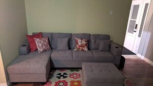 A living room with a grey sectional sofa, a matching ottoman, and a colorful floral rug. - Amazing Mattawa Riverfront, Mountain View Home, Close to Adventures & Amenities (Mattawa)