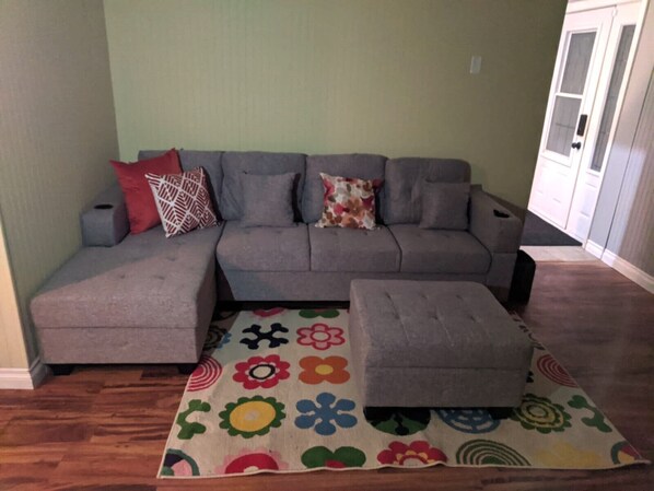 A living room with a grey sectional sofa, a matching ottoman, and a colorful floral rug.