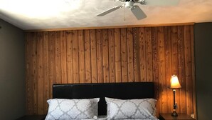 A bedroom with a wooden panel wall, a black headboard, a patterned bedspread, two nightstands, a floor lamp, and a ceiling fan. - Amazing Mattawa Riverfront, Mountain View Home, Close to Adventures & Amenities (Mattawa)
