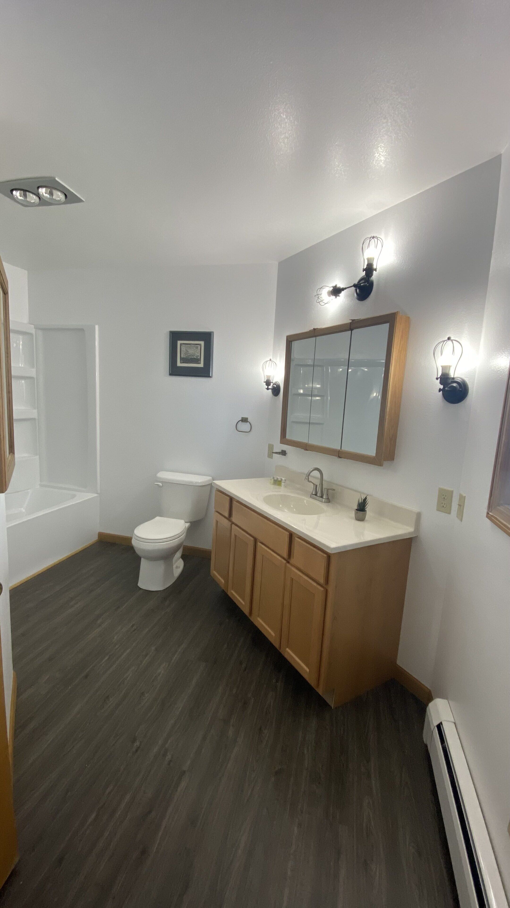 Ein modernes Badezimmer mit Badewanne, Toilette, Waschtisch und einem großen Spiegel mit Wandleuchten.