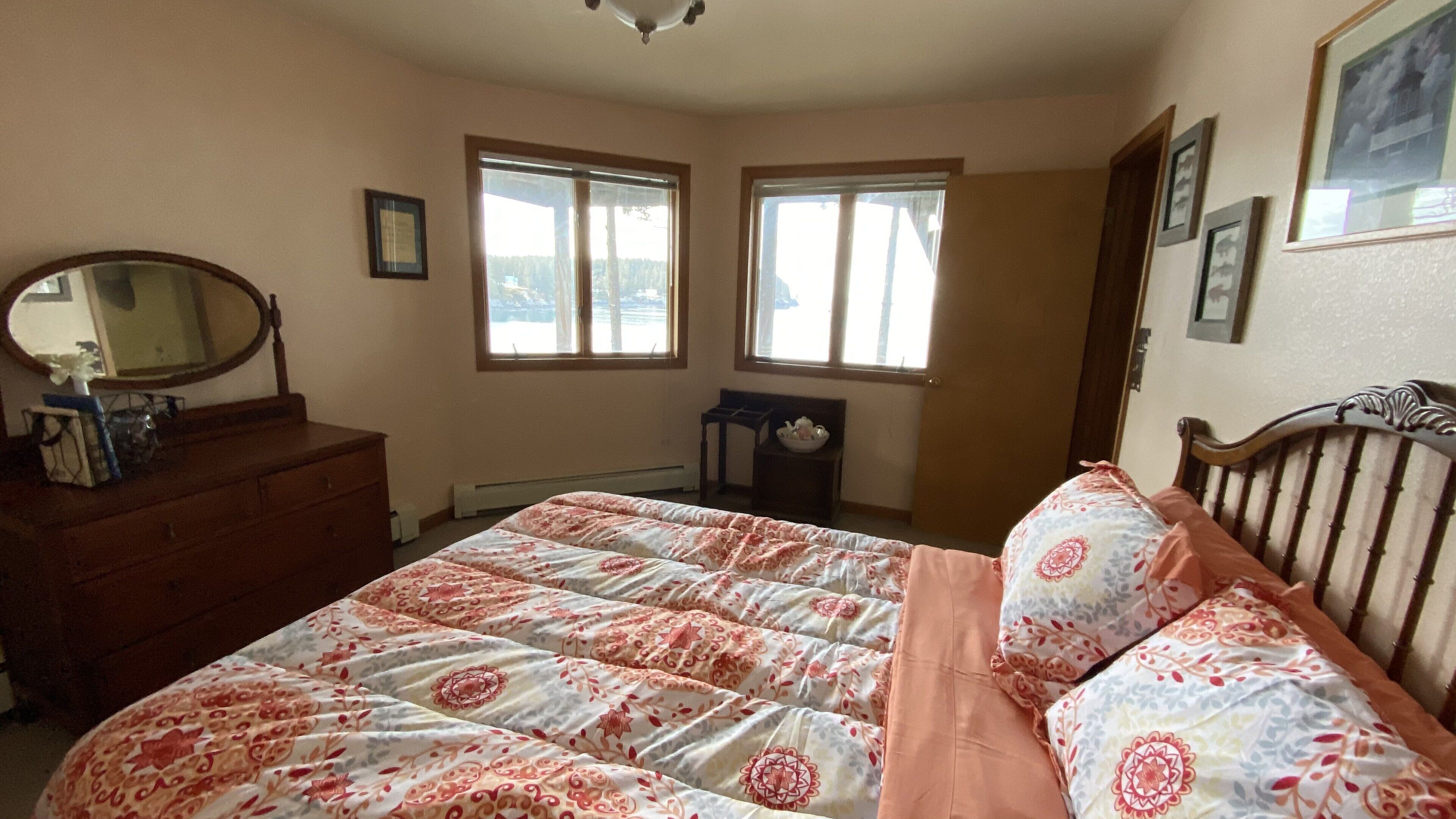 A bedroom with a bed, dresser, and two windows.