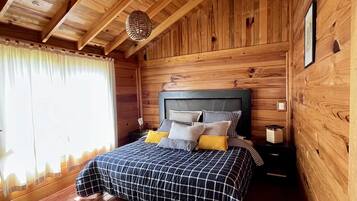 A wooden cabin bedroom with a bed, curtains, and a hanging light fixture.