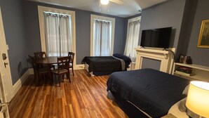 Een kamer met een bed, een bureau met stoelen, een televisie en een open haard.