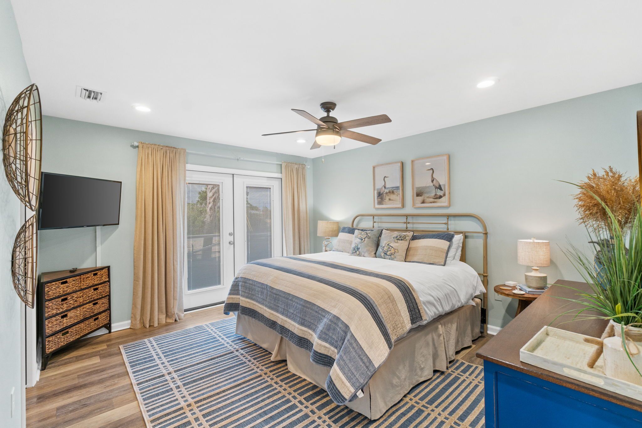 A bedroom with a bed, a ceiling fan, a TV, a dresser, and a window with curtains.