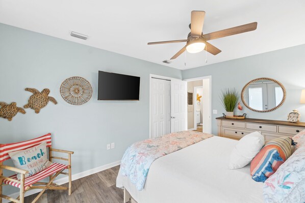 A bedroom with a bed, a chair, a dresser, a ceiling fan, a television, and decorative wall art. - Ocean View-Private Pool (Mexico Beach)