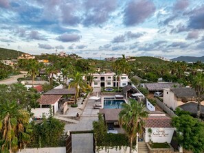 Ein Hotel mit Schwimmbad, umgeben von Palmen und einer hügeligen Landschaft.
