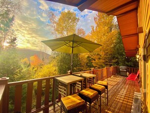 A wooden deck with outdoor seating and a large umbrella, overlooking a forested area. - Tremblant-Mont Blanc/SPA/Intimacy (St-Faustin lac carré)