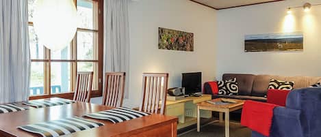 Ein Wohnzimmer mit Esstisch aus Holz, Stühlen, einer Couch und einem Fernseher.