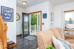 A modern interior with a wooden staircase, a beige sofa, and a welcome sign to the house. - Open year round for adventure and relaxation.  Cozy winter escape less than 20 minutes from Crystal Mountain! (Frankfort)