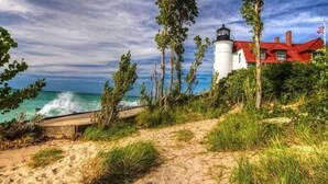 A coastal path leading to a lighthouse with a red-roofed building nearby. - Open year round for adventure and relaxation.  Cozy winter escape less than 20 minutes from Crystal Mountain! (Frankfort)