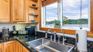 A kitchen with wooden cabinets, a stainless steel sink, a window with a view of a lake, and a countertop with a toaster and other appliances. - Open year round for adventure and relaxation.  Cozy winter escape less than 20 minutes from Crystal Mountain! (Frankfort)