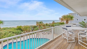 A wooden deck with a pool, outdoor furniture, and a view of the ocean.