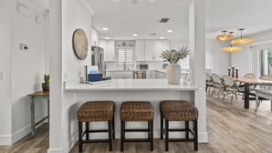 A modern kitchen with white cabinetry, a central island with stools, and pendant lighting.