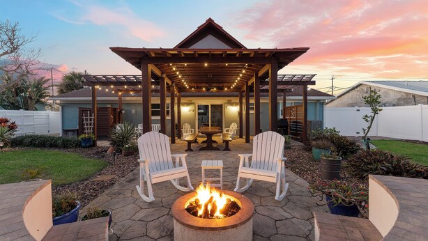 Eine Terrassenfläche mit Feuerschale, zwei weißen Adirondack-Stühlen und einer Pergola mit Lichterketten.