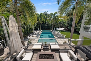 A pool area with lounge chairs and umbrellas, surrounded by palm trees and a well-maintained lawn.