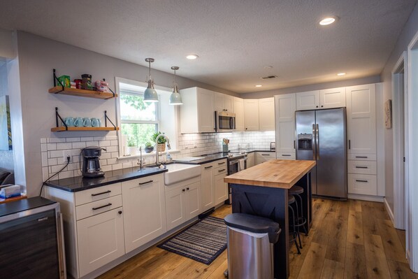 A modern kitchen with white cabinets, a stainless steel refrigerator, a wooden island, and a window with plants.