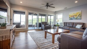 En rummelig opholdsstue med en stor sofa, et sofabord og en pejs. Der er en balkon med udsigt over landskabet.