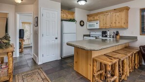 A kitchen with a central island, wooden bar stools, a refrigerator, a stove, and wooden cabinets. - Mountain Condo Near Snowbasin, Powder & Nordic (Eden)
