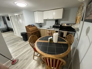 A compact kitchen with white cabinets, a black countertop, and a dining area with a round table and wooden chairs.