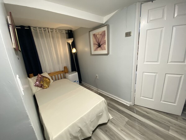 A bedroom with a bed, a nightstand, a lamp, a door, and a wall-mounted picture.