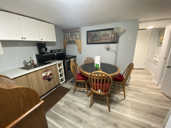 A compact kitchen with wooden cabinets, a dining table with chairs, and a painting on the wall.
