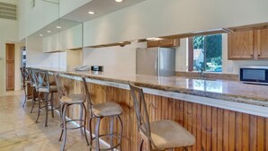 Una cocina moderna con una encimera larga, taburetes de bar y un refrigerador de acero inoxidable.