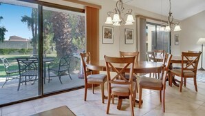 Comedor con una gran mesa y sillas, un candelabro y un puerta corrediza de vidrio que da a un patio exterior.