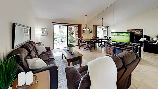 Un salón amplio con un sofá grande, una mesa de centro y una televisión. Hay un comedor con sillas y una mesa, y un ventanal que proporciona luz natural.