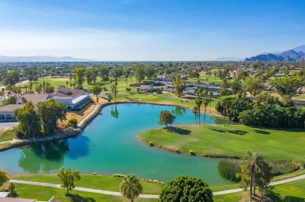 A golf course with a pond, surrounded by greenery and buildings.