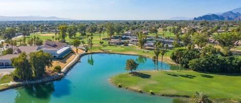 A golf course with a pond, surrounded by greenery and buildings.