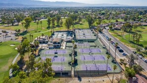 Vista aérea de un complejo de tenis con varias canchas, rodeado de zonas residenciales y vegetación.