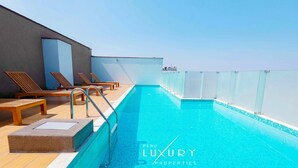 Una piscina en la azotea con sillones de descanso y cielo despejado.
