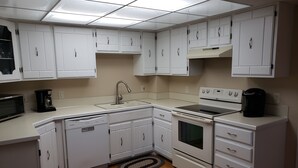 A compact kitchen with white cabinets, a dishwasher, an oven, a microwave, and a coffee maker. - Spacious SW Omaha Home Near I-80, Garage Game Room, Family-Friendly, Safe Area! (Omaha)