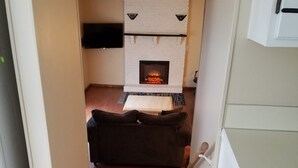 A narrow hallway leading to a living area with a fireplace, a sofa, and a wooden floor. - Spacious SW Omaha Home Near I-80, Garage Game Room, Family-Friendly, Safe Area! (Omaha)