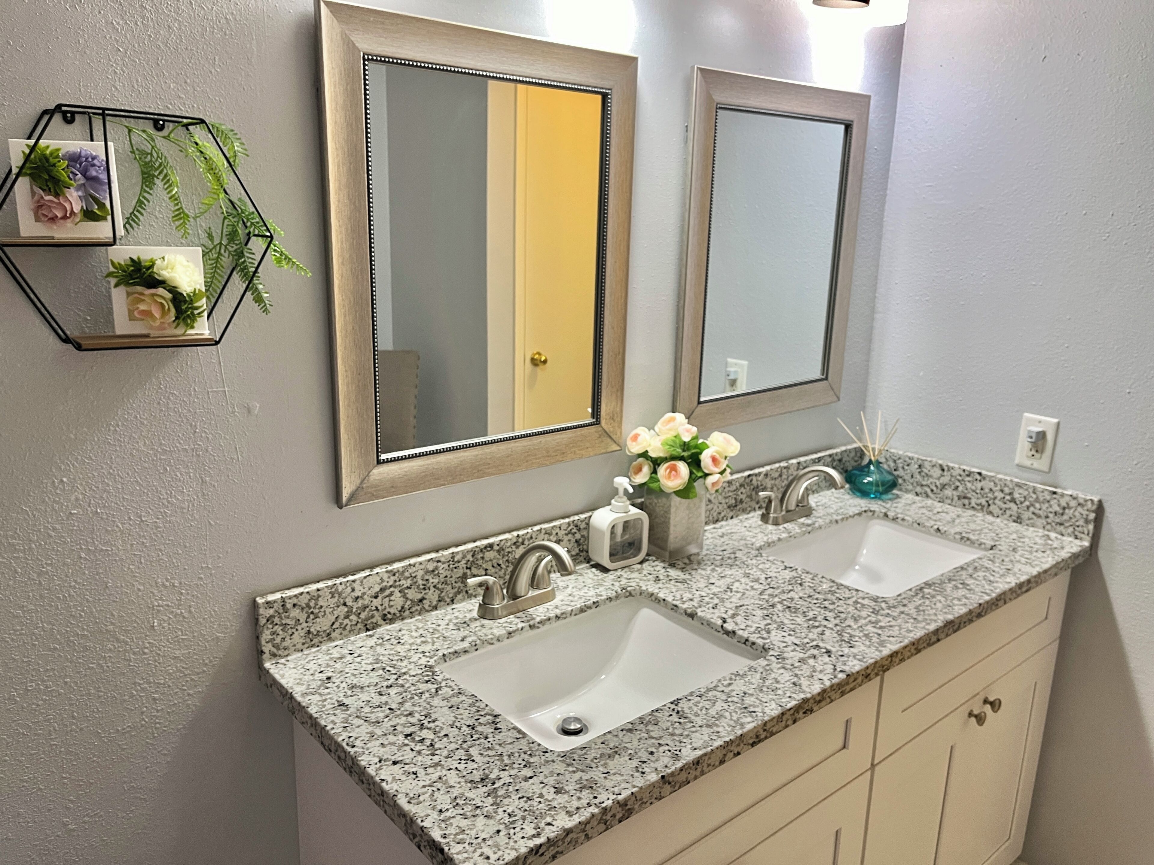 Un baño con dos lavamanos, un espejo y un adorno hexagonal en la pared.