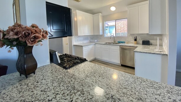 A kitchen with white cabinets, a granite countertop, a stove, and a window with a view of a brick wall. - 4110 David & Jennie’s Place (Missouri City)