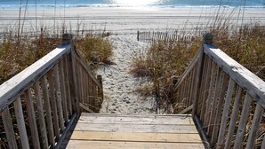 A wooden boardwalk leading to a beach with sand and grass on either side. - Portofino I 1424 - Oceanfront in Garden City Beach (Garden City Beach)
