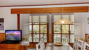 Un comedor con una mesa de madera, sillas blancas y un televisor sobre un mueble de madera.