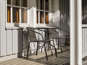 Eine Terrasse mit zwei Metallstühlen und einem Tisch, weißen Außenwänden und einem Fenster mit Jalousien.